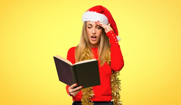 Mujer rubia vestida para las vacaciones navideñas sosteniendo un libro y sorprendida mientras disfruta