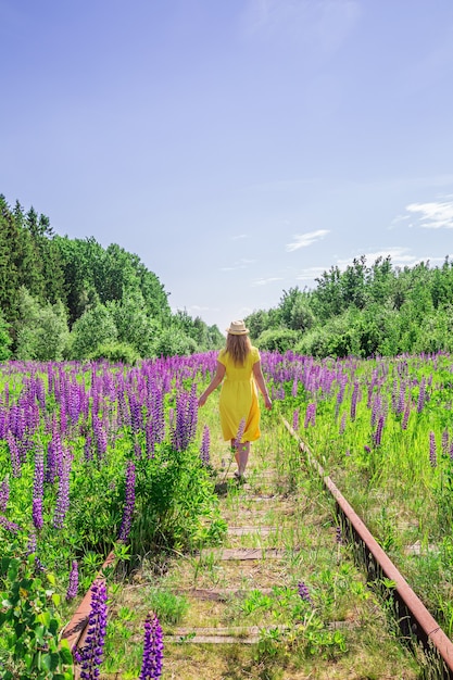 Mujer rubia con un vestido amarillo en campo de altramuces. Día soleado de verano. Relajación, vacaciones, concepto de libertad.