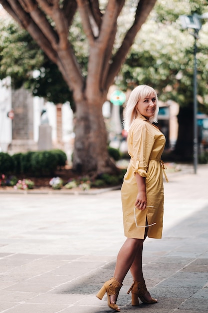 Una mujer rubia con un vestido amarillo de verano se encuentra en la calle del casco antiguo de La Laguna en la isla de Tenerife, España, Islas Canarias.