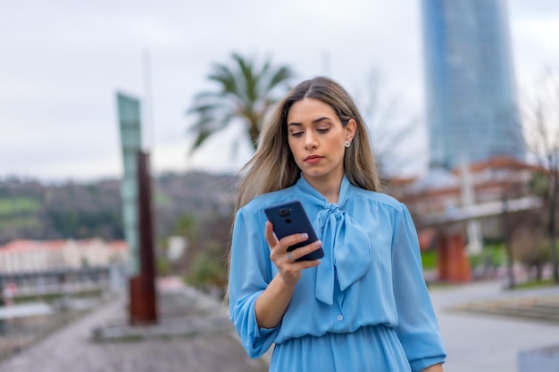 Mujer rubia con vestido azul hablando por teléfono caminando en el concepto de estilo de vida de la ciudad