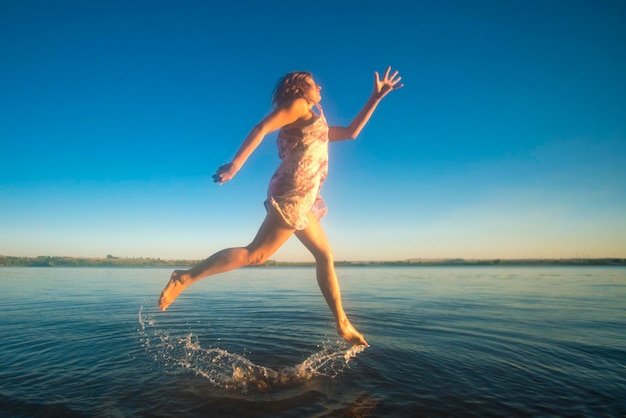 Mujer rubia con un vestido corriendo por el agua en el fondo del cielo azul