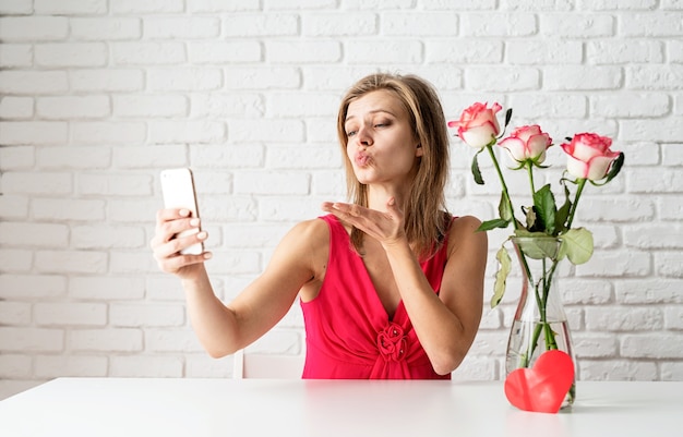 mujer rubia en vestido rosa que data en línea enviando besos a sus novios