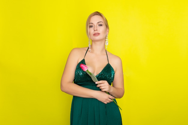 Mujer rubia en vestido verde con un tulipán rosa