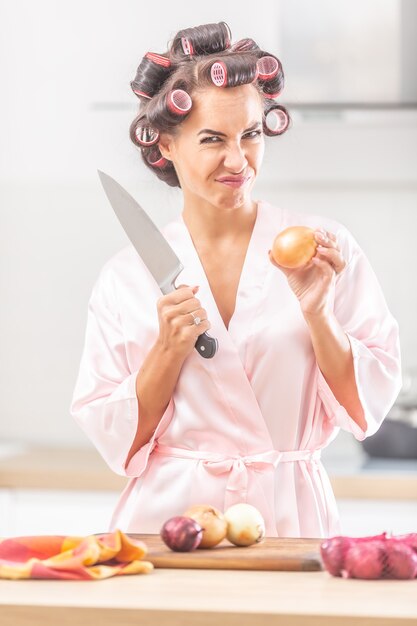 Mujer con rulos y pijama de seda frunce el ceño ante la necesidad de cortar la cebolla con un cuchillo.