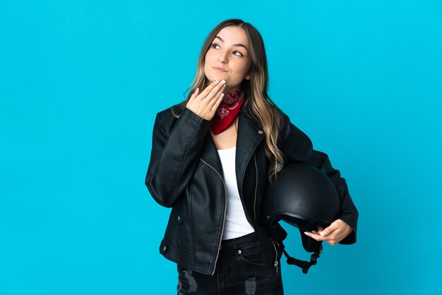 Mujer rumana sosteniendo un casco de motocicleta aislado en azul mirando hacia arriba mientras sonríe