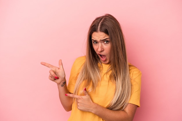 Mujer rusa joven aislada sobre fondo rosa tiene espacio de copia en una palma, mantenga la mano sobre la mejilla. Asombrado y encantado.