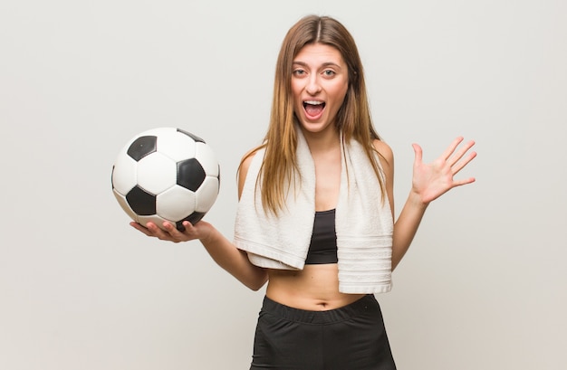 Mujer rusa joven fitness celebrando una victoria o un éxito. Sosteniendo un balón de fútbol.