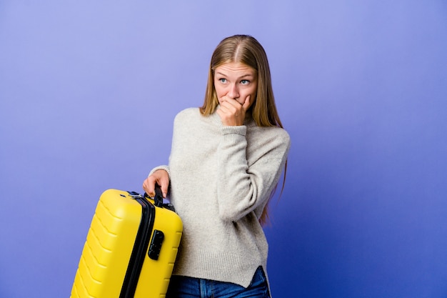 Mujer rusa joven que sostiene la maleta para viajar pensativo mirando a un espacio de copia cubriendo la boca con la mano.