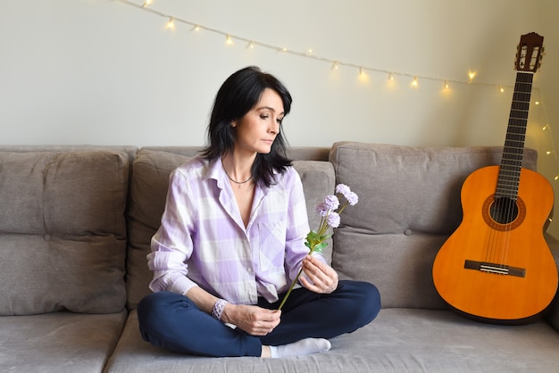 Mujer rusa molesta mirando flores lilas y sentado en el sofá en casa