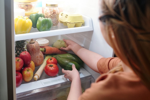 Foto mujer sacando calabacín fresco de la nevera para hacer un plato delicioso y saludable para la cena