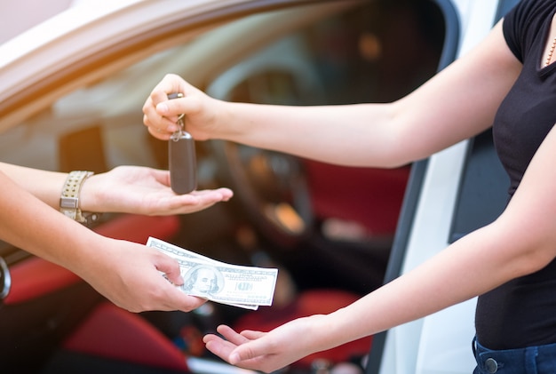 Mujer en la sala de exposición dando dólares de dinero y tomando las llaves del coche