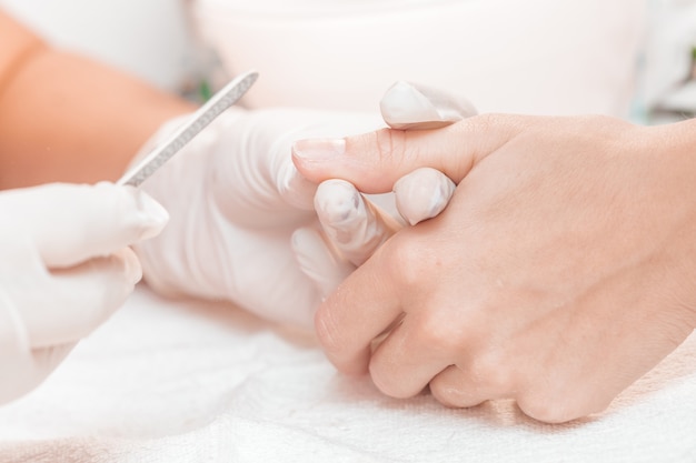 Mujer en un salón de belleza recibiendo una manicura por una esteticista con lima de uñas.