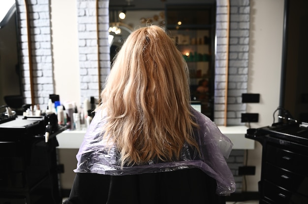 Una mujer en un salón de belleza se sienta en una silla de peluquería con el pelo suelto, esperando ser tratada.