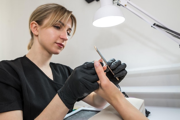 Una mujer en un salón de uñas haciéndose la manicura por una cosmetóloga con una lima de uñas