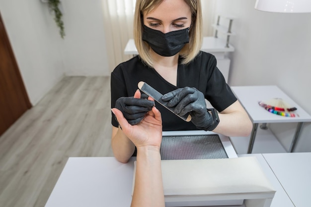 Una mujer en un salón de uñas haciéndose la manicura por una cosmetóloga con una lima de uñas