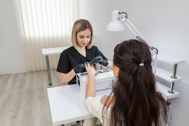 Una mujer en un salón de uñas haciéndose la manicura por una cosmetóloga con una lima de uñas