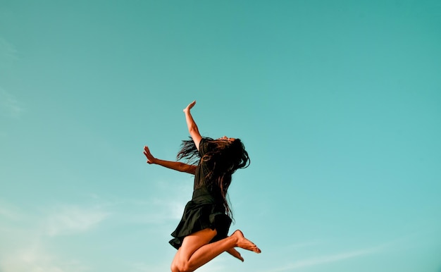 Mujer saltando con los brazos levantados contra el cielo.