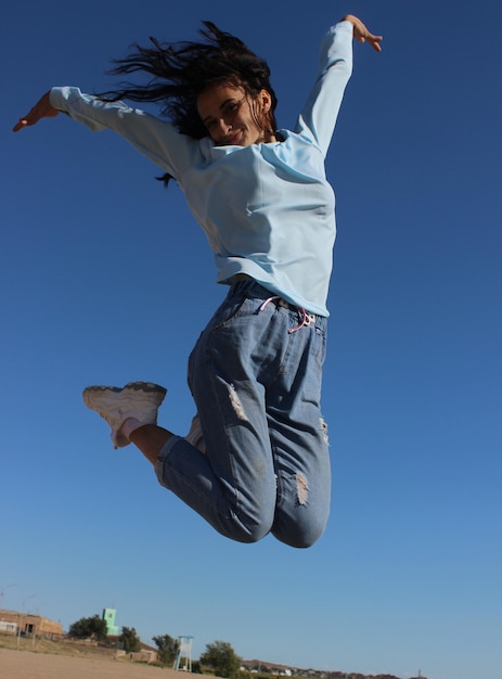 Mujer saltando contra el cielo azul claro