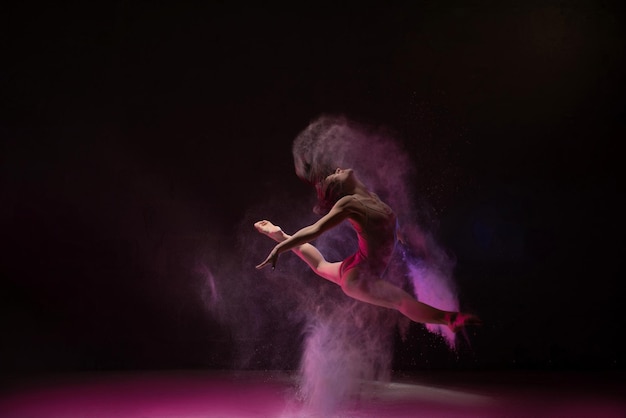Mujer saltando con gracia en la nube de polvo de color
