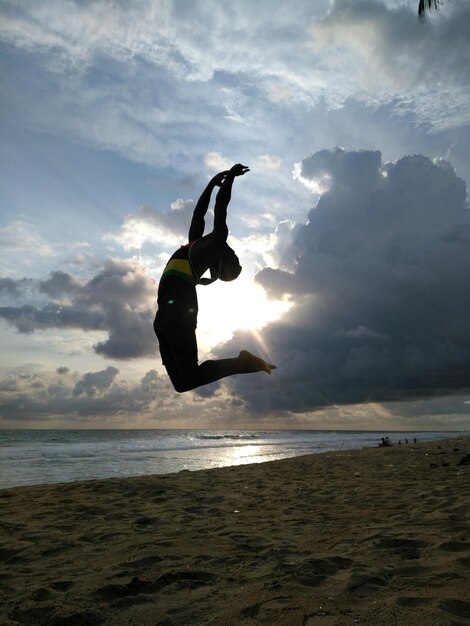 Foto mujer saltando en la playa contra el cielo durante la puesta de sol