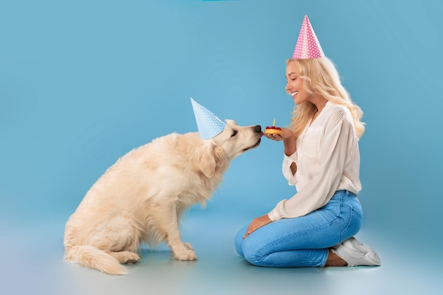 Mujer saludando a un lindo perro sano con gorro de fiesta con pastel