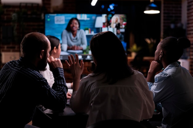 Foto mujer saludando en videoconferencia en línea con empresario afroamericano y colegas que trabajan a distancia desde casa. los compañeros de trabajo saludan a los clientes de la empresa en una llamada por internet en una reunión nocturna.