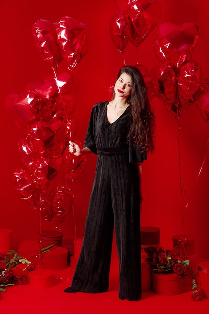 Mujer de San Valentín en negro con globos rojos en forma de corazón divirtiéndose