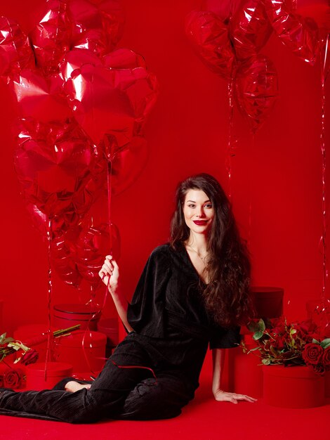 Mujer de San Valentín en negro con globos rojos en forma de corazón divirtiéndose