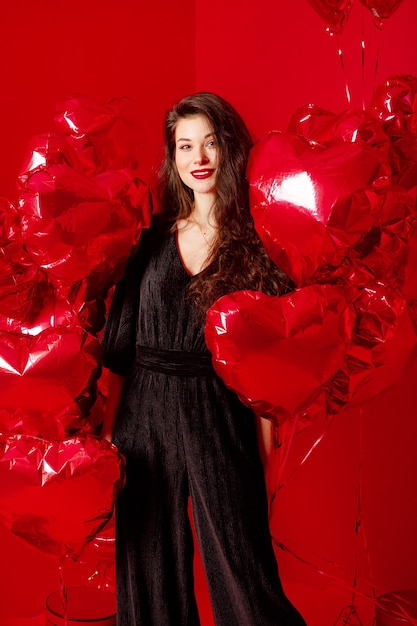 Mujer de San Valentín en negro con globos rojos en forma de corazón divirtiéndose