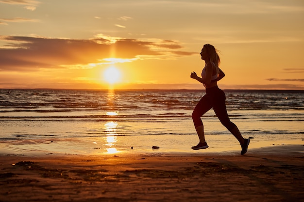 Mujer sana corre al aire libre durante la puesta de sol cerca de la costa