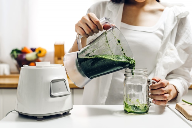 Mujer sana disfruta haciendo jugo verde con verduras y frutas verdes con licuadora