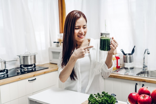 La mujer sana disfruta haciendo que la desintoxicación de las verduras verdes limpia y el licuado de la fruta verde con la licuadora en cocina en casa. Concepto de dieta. estilo de vida saludable