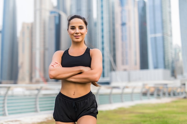 Mujer sana joven que se relaja después de hacer aptitud en el puerto deportivo de Dubai con los rascacielos en el espacio.