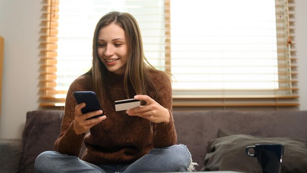 Mujer satisfecha con tarjeta de crédito y compras en línea en su teléfono inteligente