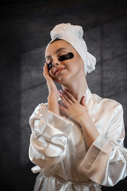 Mujer satisfecha con toalla blanca aplicando parches en los ojos para las arrugas hinchadas