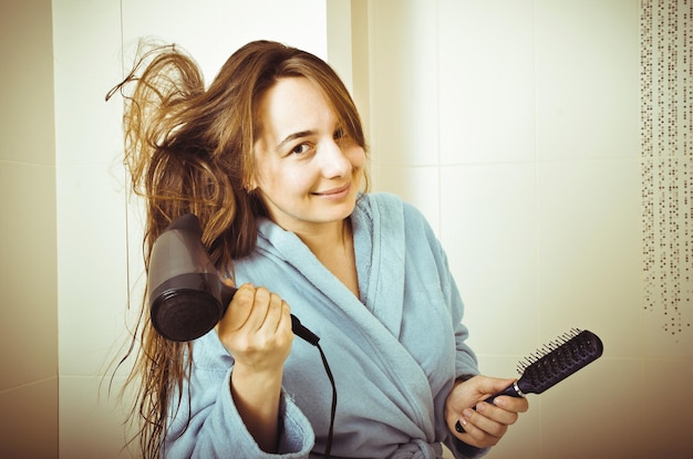 Mujer con secador de pelo en un baño.