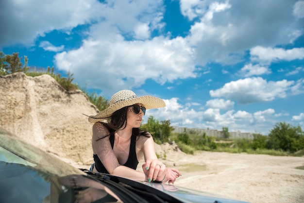 Mujer seductora posando junto al coche en verano fuera de la ciudad disfrutando de la libertad