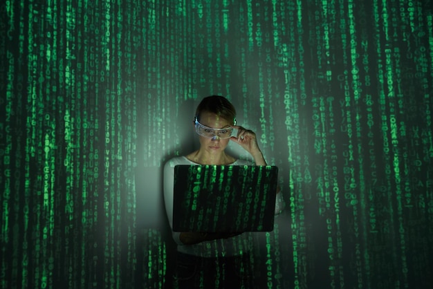 Mujer segura ajustando gafas futuristas mientras usa una computadora portátil contra un fondo oscuro