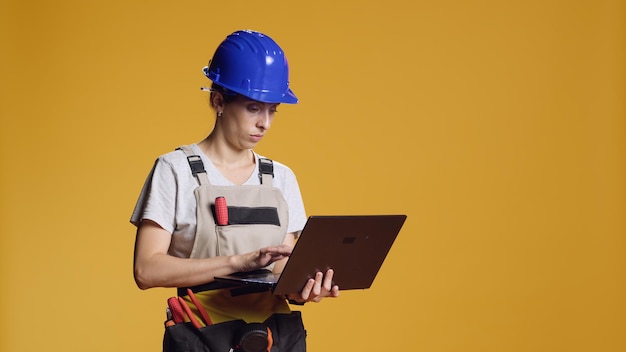 Mujer segura de sí misma navegando por Internet en una computadora portátil, encontrando inspiración de construcción para trabajar en un trabajo de construcción atípico. Handywoman usando computadora en estudio, trabajando en remodelación industrial.