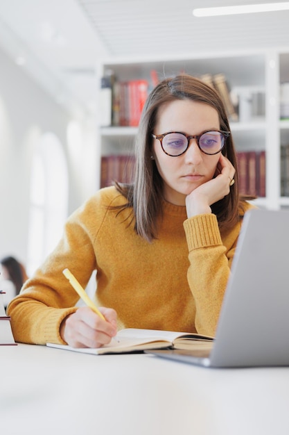 Mujer segura trabaja en la biblioteca en coworking en la computadora portátil o en la oficina estudiante está estudiando en línea