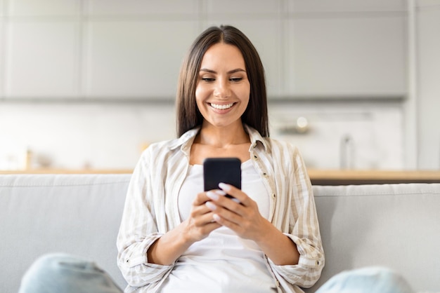 Mujer segura usando teléfono inteligente y sonriendo en casa