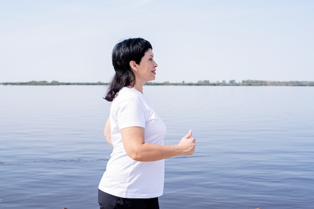 Mujer senior activa para correr cerca de la orilla del río