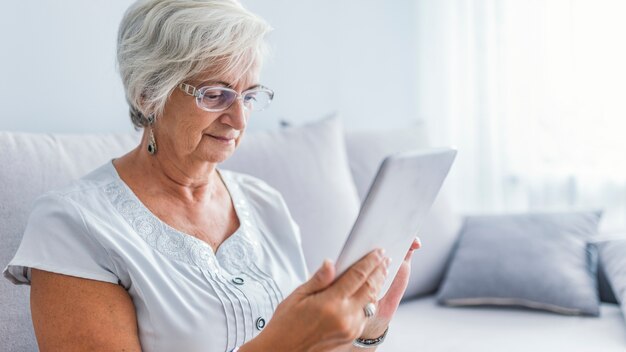 Mujer Senior con anteojos navegando en tableta digital