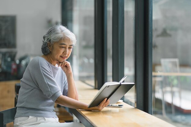 Mujer senior asiática leyendo un libro mientras se relaja en una cafetería