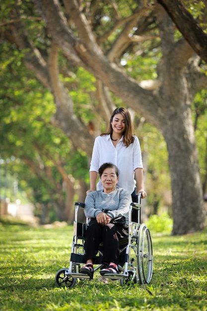 Mujer senior asiática sentada en la silla de ruedas con su hija hija feliz sonrisa cara en el parque verde