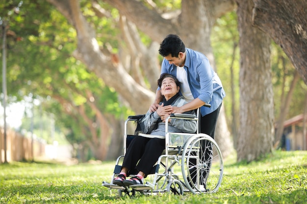 Mujer senior asiática sentada en la silla de ruedas con su hijo sonrisa feliz cara en el parque verde