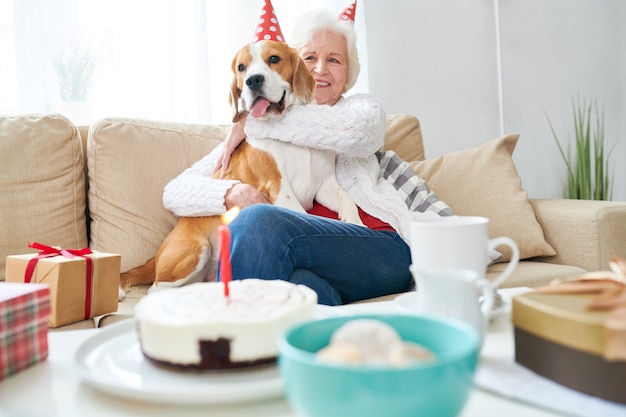 Mujer senior feliz abrazando a perro en cumpleaños