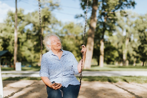 Mujer senior feliz escuchando música en un columpio