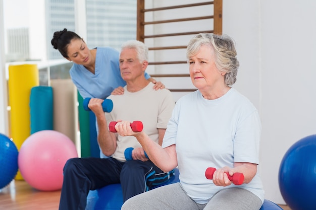 Mujer Senior levantando pesas con hombre y entrenador en el gimnasio