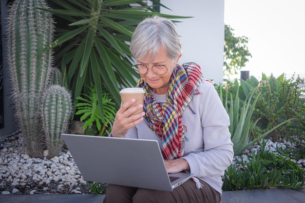 Mujer senior madura sonriente relajada usando una computadora portátil fuera de casa sentada en el jardín
